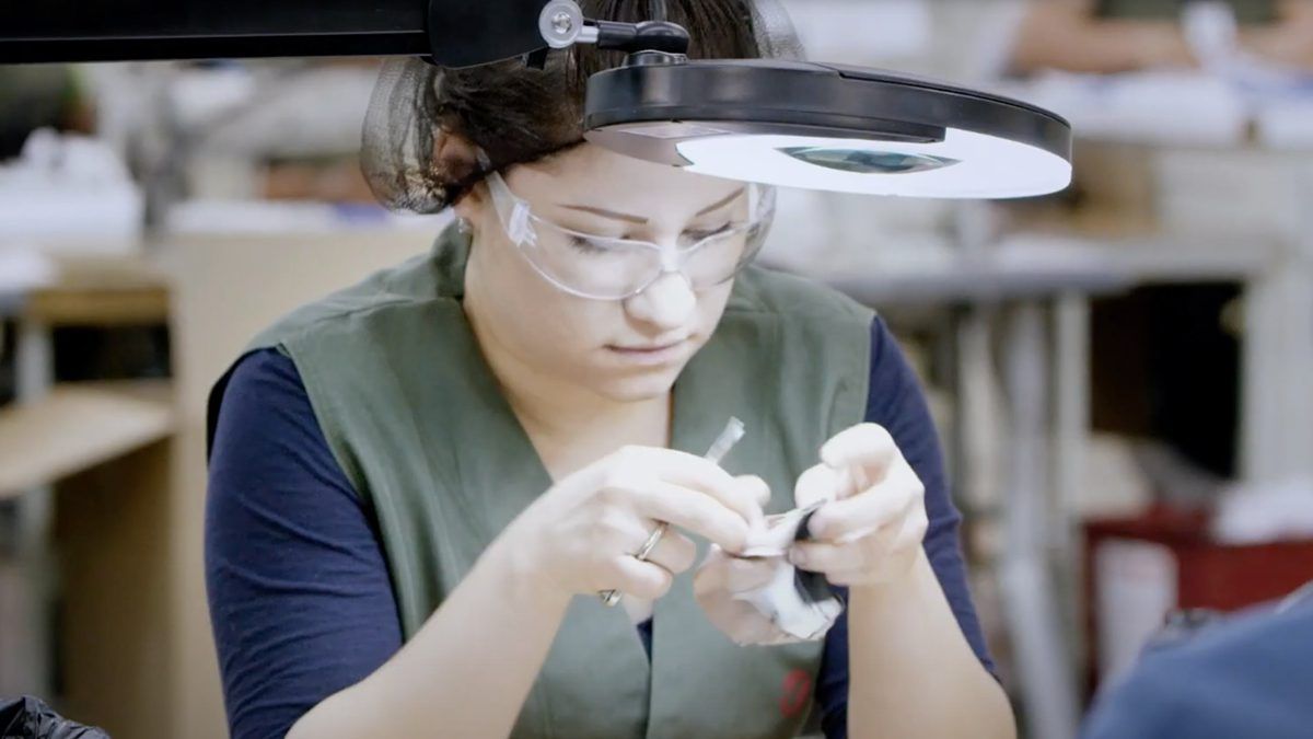 Woman in protective goggles with overhead light, looking closely at hook and loop