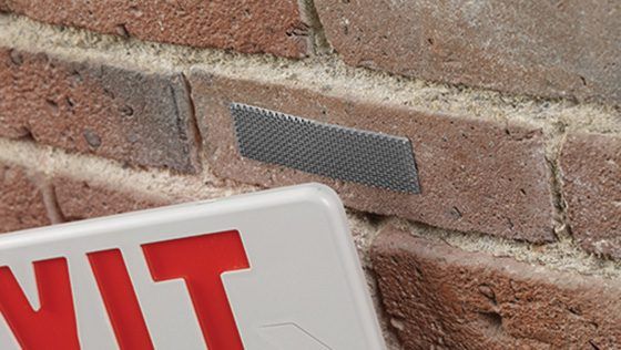 Close-up of a red and white EXIT sign being mounted on a brick wall using VELCRO® Brand fasteners, offering a secure, no-drill solution.