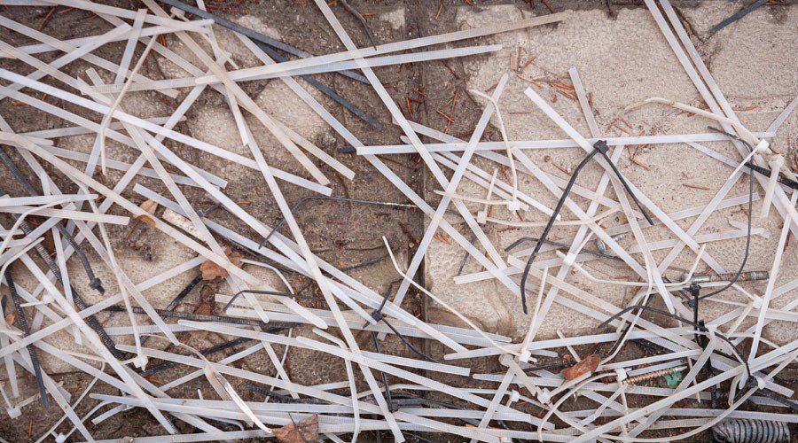 Discarded white and black plastic zip ties scattered on the ground, illustrating the waste created by single-use fasteners and the need for reusable hook and loop alternatives in the manufacturing process.