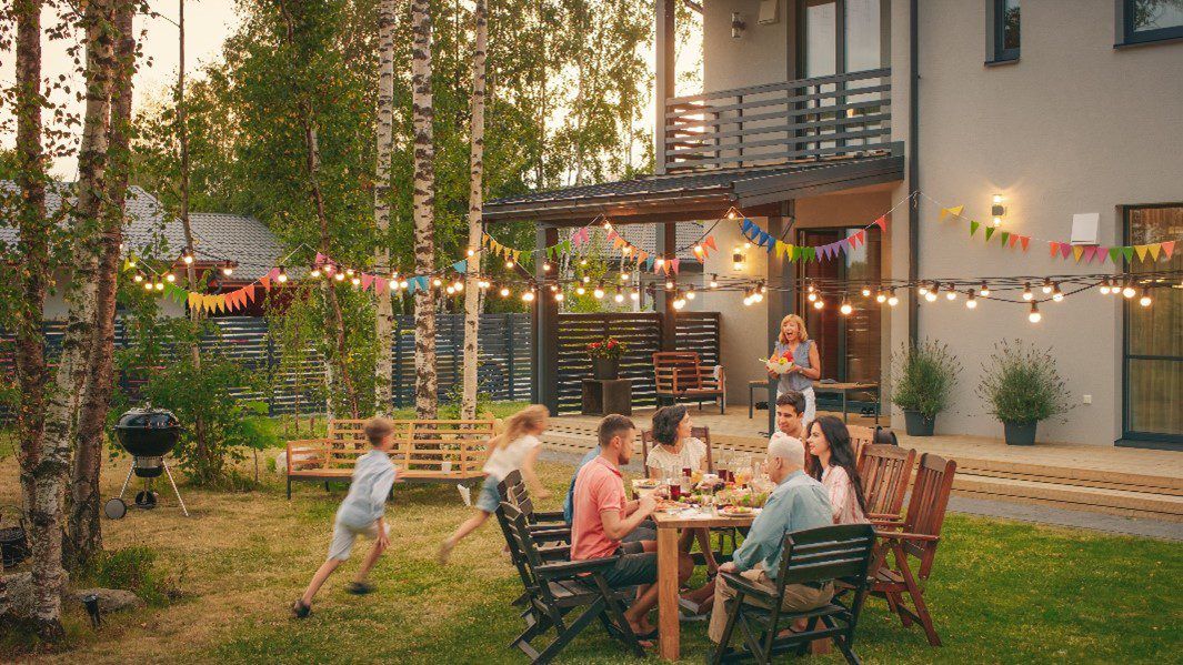 A family enjoying dinner in the backyard. lights and flags are strung about