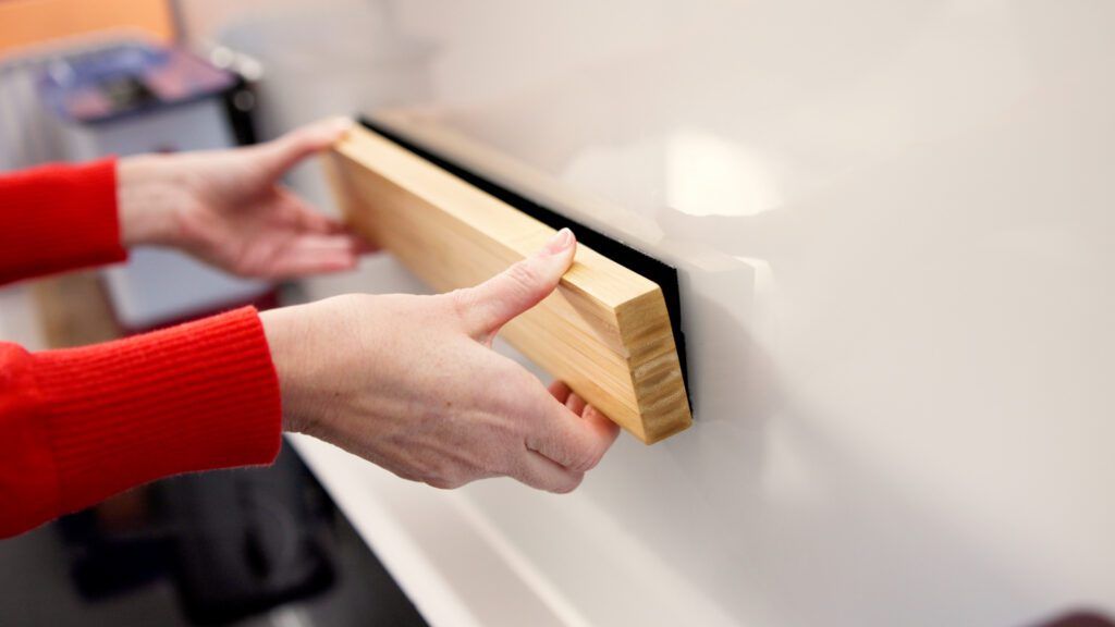 Hands sticking magnetic knife rack to wall using VELCRO® Brand Kitchen & Bath Mounting Tape