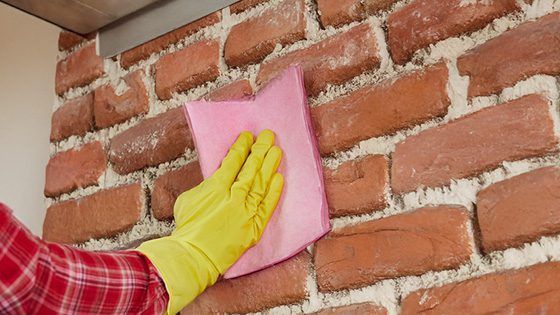 Person wearing a yellow rubber glove cleaning a reddish-brown brick wall with a pink cloth. Preparing the surface for applying VELCRO® Brand fasteners.